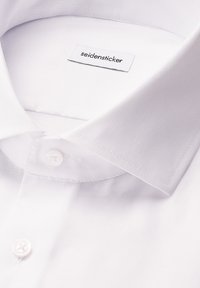 Witte overhemdbloes met een klassieke kraag en twee witte knopen, waarin een "seidensticker" merklabel binnen de kraag zichtbaar is.