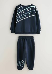 Dunkelblaues Sweatshirt- und Hosen-Set aus weichem Stoff. Das Sweatshirt hat ein diagonal verlaufendes weißes und hellblaues Schriftmuster; die Hose trägt ein ähnliches Muster.