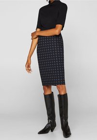 Svart kortärmad topp i kombination med en knälång marinblå blyertskjol med rutmönster, kompletterad med eleganta svarta knähöga stövlar.