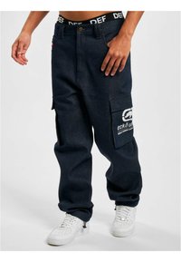Navy denim cargo pants with a loose fit, featuring pockets and a white logo detail. Pairing with white sneakers and a contrasting waistband.