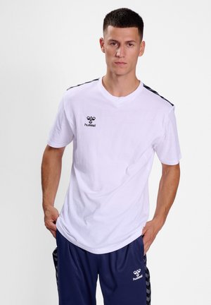 T-shirt en coton blanc à manches courtes, avec des accents noirs sur les épaules et un petit logo sur la poitrine.