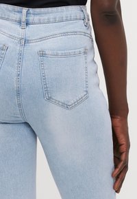 Jeans de mezclilla azul claro con una textura suave, de cintura alta, y bolsillos traseros que presentan un sutil detalle de costura en forma de V.