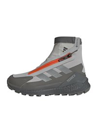 Grey and white mid-cut hiking shoe with orange zippers, textured synthetic upper, a rugged sole, and prominent TERREX branding.