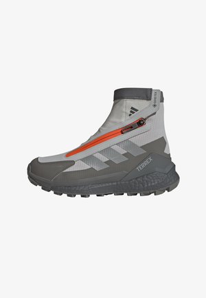 Chaussure de randonnée mi-haute grise et blanche avec des fermetures éclair orange, une tige synthétique texturée, une semelle robuste et un marquage TERREX bien visible.