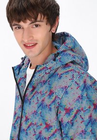 Giacca multi-colore e a fantasia con cappuccio, chiusura con zip e una consistenza simile a rete con punti blu, rosa e bianchi.