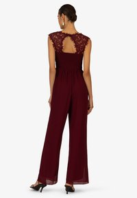 Burgunderfarbener Jumpsuit mit Spitzenärmeln, gerafftem Oberteil und weit geschnittenen Hosenbeinen. Verfügt über ein Rückenausschnitt-Detail und einen weichen, fließenden Stoff.