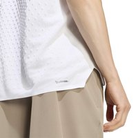 Gros plan d'une personne portant une chemise blanche texturée étiquetée "Climacool" et un pantalon beige, avec son bras droit détendu le long du corps.
