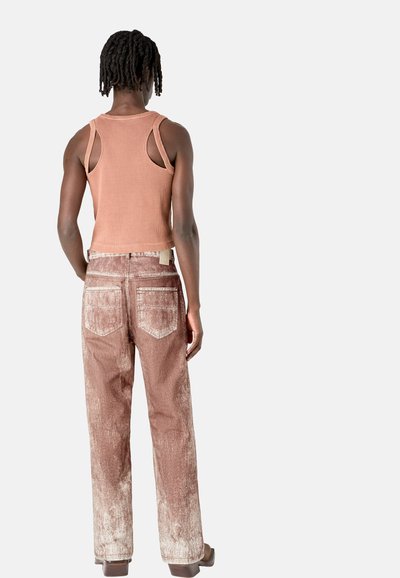Ribbed, sleeveless, peach tank top paired with faded, rust-colored, wide-leg jeans. Notable back pocket design and texture details.