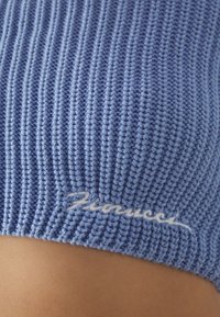 Tissu en jersey bleu tricoté avec une texture côtelée, présentant un logo brodé blanc en bas. Fini lisse avec une apparence douce et extensible.