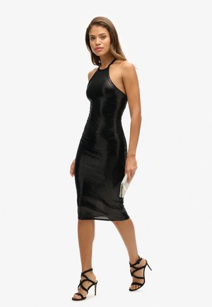 Czarna sukienka do połowy łydki z cekinami, dopasowana w szyję w kształcie halter, o gładkiej fakturze, zestawiona z czarnymi sandałami na wysokim obcasie z paskami i małą kopertówką.