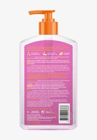 Clear plastic pump bottle with orange dispenser, containing pink tanning gel, showing detailed application instructions and ingredient list on back label.