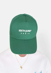 Grüne Baseballmütze mit strukturiertem Design. Auf der Vorderseite mit weißem, gesticktem Text: "SIXTH JUNE PARIS". Glatte Stoffoberfläche.