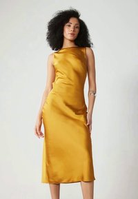 Abito in satin giallo con una silhouette aderente e slanciata, caratterizzato da un collo a barca e una fessura laterale, che offre una texture liscia e lussuosa.