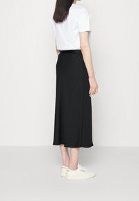 Jupe midi noire au tissu lisse, avec une taille ajustée et de légentes fentes sur les côtés, associée à un t-shirt blanc à manches courtes et des baskets blanches.