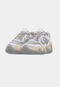 Ζευγάρι λευκά και γκρι αθλητικά παπούτσια με μπεζ κυματιστή σόλα και λογότυπο αστεριού στο πλάι, εμφανιζόμενα από μπροστινή γωνία σε απλό φόντο.