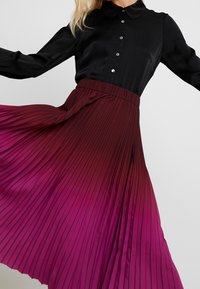 Schwarzes Hemd mit Kragen und Knopfleiste, kombiniert mit einem plissierten Rock in Farbverlauf von Tiefrot zu Hellrosa, mit glatter Textur.