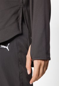 Svart idrottströja med långa ärmar, med en manschettkant och en sid_slits, tillverkad av mjukt och flexibelt tyg. Puma-logotyp i vitt.