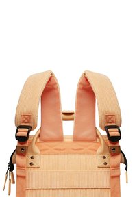 Zaino in corduroy arancione con spallacci imbottiti e regolabili, dettagli con cerniera e hardware in metallo. Presenta una superficie testurizzata e una costruzione solida.