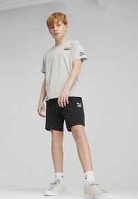 T-shirt grigio in cotone con un piccolo logo sul petto, abbinato a pantaloni corti neri con un logo sull'orlo, indossato con calze e scarpe bianche.