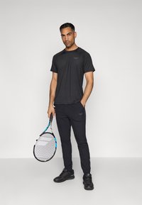 Melnas sporta krekls un melnas bikses, izgatavotas no viegla auduma. Turētājs tenisam ar zilām akcentiem, ģērbies melnās kurpēs.