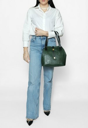 Borsa a mano verde con texture a motivo esagonale, manici neri, accessori dorati e una forma strutturata. Indossata con jeans a vita alta blu chiaro.