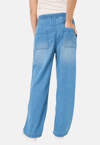 Světle modré denimové kalhoty širokého střihu s páskem na stažení, dvěma zadními kapsami a uvolněným střihem, s hladkou texturou a ležérním designem.