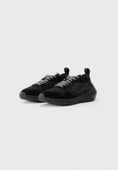 Black athletic shoes with mesh and suede materials. Textured black outsoles with white speckles. Reflective laces and heel tab for easy wear.