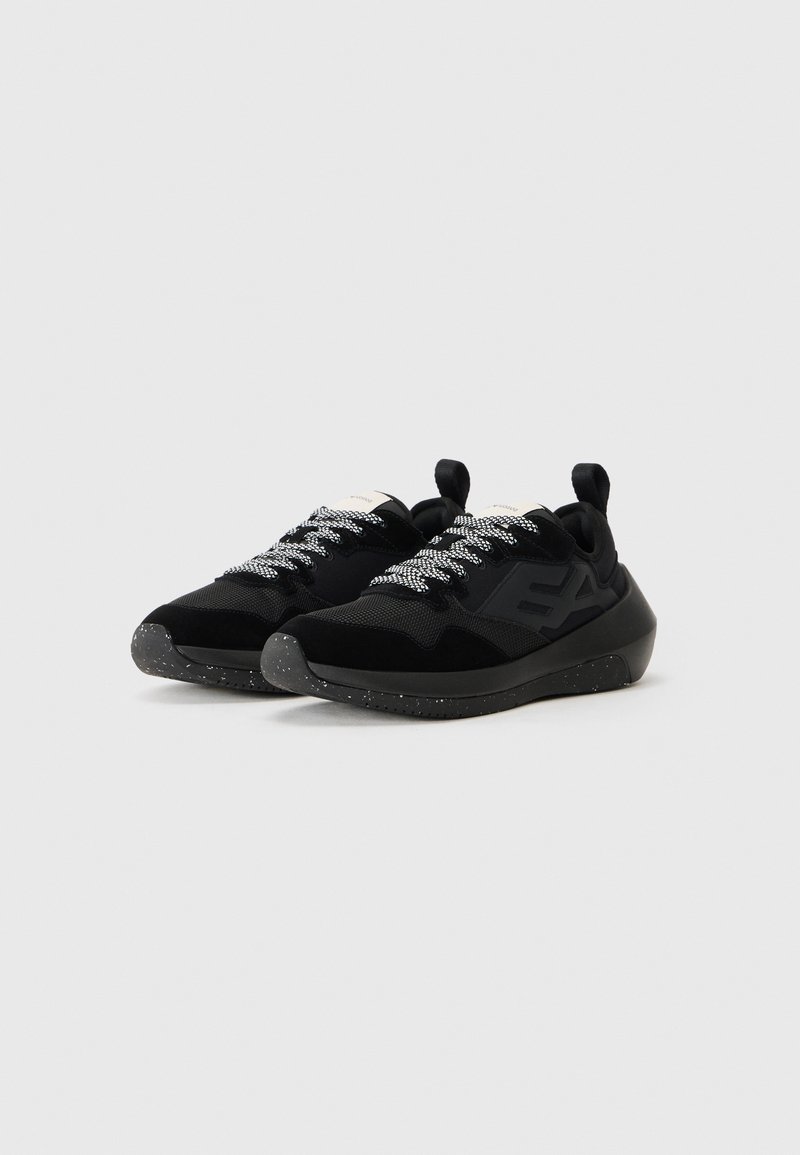 Zapatillas deportivas negras con materiales de malla y ante. Suelas exteriores negras texturizadas con manchas blancas. Cordones reflectantes y una pestaña en el talón para facilitar su uso.