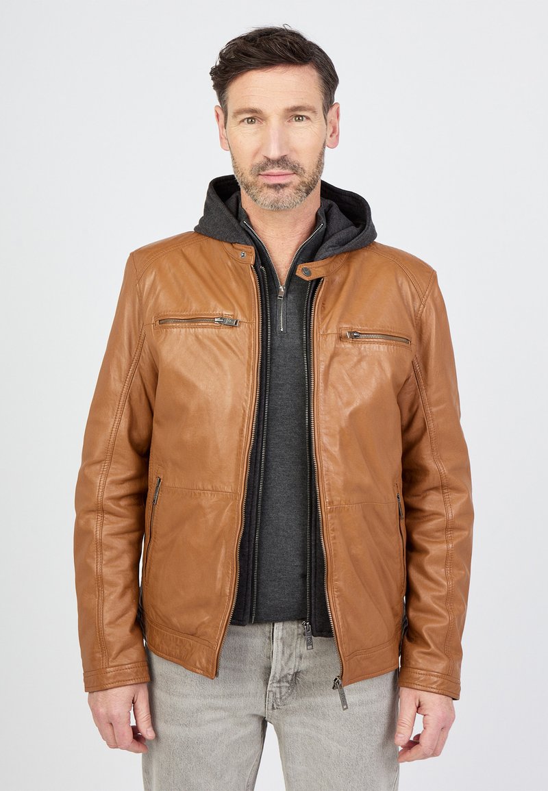 Brun læderjakke med frontlynlås, to lynlås brystlommer og en grå hættetrøje under. Glat tekstur, tætsiddende design.