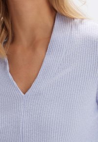 Ljusblå V-ringad ribbstickad tröja med mjuk textur och figursydd design. Närbild med fokus på halsringningen och tygdetaljer.