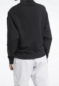 Sudadera negra con cuello alto y corte relajado, que presenta mangas largas y puños acanalados. Combinada con pantalones blancos texturizados.
