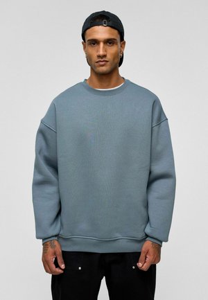 Lichtblauwe sweatshirt met een geribbeld oppervlak, ronde halslijn en verlaagde schouders. Gecombineerd met zwarte broek, zonder zichtbare patronen of metalendetails.