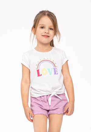 Camiseta blanca de manga corta con "LOVE" en letras multicolores y diseño de arcoíris; combinada con pantalones cortos desgastados de color lila claro con un lazo.