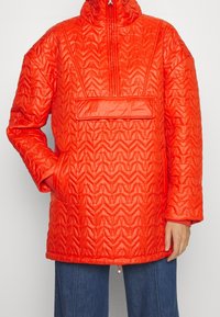 Czerwona pikowana bluza na suwak z wysokim kołnierzem, posiadająca przednią kieszeń, fakturowany wzór oraz elastyczny sznurek ściągający u dołu.