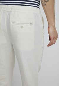 Pantalones de lino blancos con un bolsillo trasero que cuenta con un cierre de botón y un sutil acento negro. Cintura elástica para mayor comodidad. Textura suave.