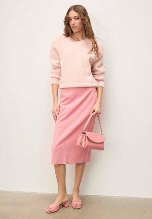 Pull en maille rose avec manches ballon, associé à une jupe midi rose ajustée. Accessoires comprenant un sac à main rose assorti et des sandales à enfiler.