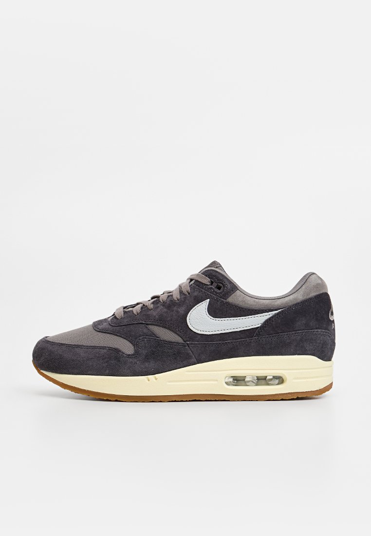 Nike Air Max sneaker in donkergrijs suede en mesh, crèmekleurige tussenzool met zichtbare luchtunit, gumrubberen buitenzool, lichtblauwe swoosh-detail.