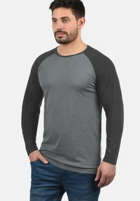 Camicia a maniche lunghe con corpo grigio e maniche raglan grigio scuro, realizzata in tessuto morbido con design aderente. Piccolo logo in accentuazione sul lato.