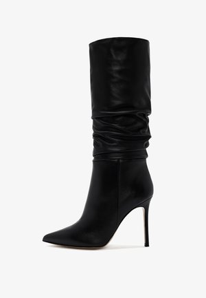 Botte en cuir noir à talons hauts avec un embout pointu, un tige en cuir souple et une silhouette élégante. Possède un talon aiguille et une texture lisse.