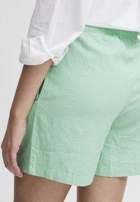 Pantaloni corti di cotone verde chiaro con cintura elastica, tasche laterali e vestibilità rilassata. L'orlo ha una finitura semplice e pulita.