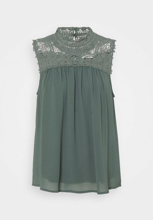 Mouwloze groene blouse met hoge kanten kraag en kanten detail over de schouders, vloeiende geplooide stof eronder en een keyhole knoopsluiting aan de achterkant.