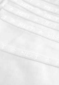 Weiße Baumwollunterwäsche mit auffälligem Logo-Bund, ausgestattet mit subtiler Textur und glattem Finish. Acht Stück gestapelt mit sichtbarem Branding-Detail.