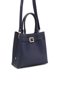 Námornícky modrá kabelka vyrobená z hladkého materiálu, s dvojitými uchami, odnímateľným popruhom a zlatým prackovým akcentom na prednej strane.