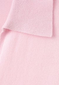 Tissu tricoté rose doux avec un revers plié montrant une fine texture côtelée sur le bord et un tricot lisse en dessous.