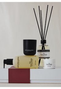 Ensemble de quatre produits : une bougie noire, un diffuseur transparent avec des bâtonnets, un gel douche jaune et une crème pour le corps blanche, tous étiquetés "Rock Roses".