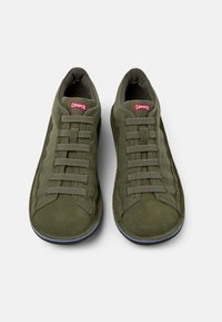 Green suede sneakers with a rounded toe, featuring a lace-up design and textured side panels. Red logo on the tongue, flat rubber sole.