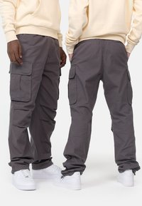 Cargo pants in dark gray fabric, featuring side pockets, loose fit, and elastic cuffs, paired with white sneakers.
