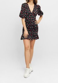 Schwarzes Kleid mit floralen Muster, das kurze puffärmel, einen tiefen V-Ausschnitt, Raffung und einen gerüschten Saum aufweist.