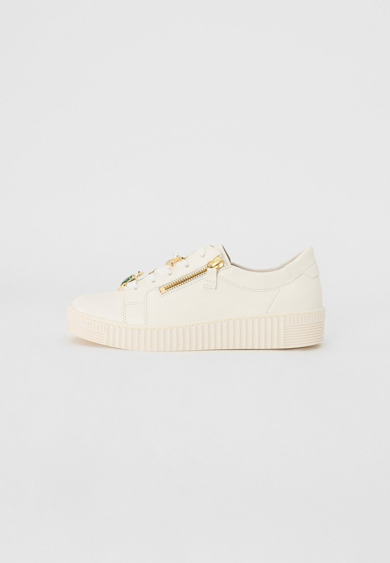 Zapatillas de piel blanca con suela plana, que presentan cremalleras decorativas, cordones en la parte frontal y detalles acanalados a lo largo de la suela.