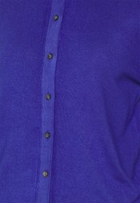 Fioletowa koszula na guziki z prążkowanej tkaniny, z rzędem ciemnych guzików i gładką teksturą z przodu.